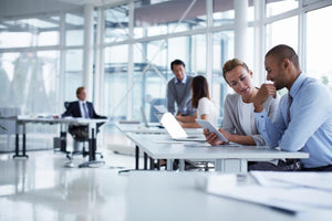 An office. The picture is mainly focused on a man and a woman looking at a tablet together.