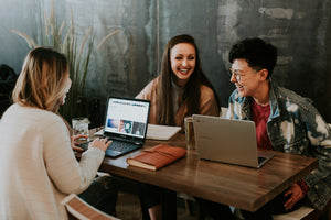 Three woman laughing together at a table with tablets.