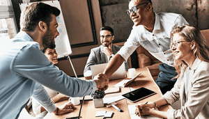 A group meeting in a cafe or an office. Two men shaking hands.