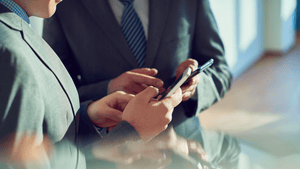 A picture of two people in suits, showing each other their phones.