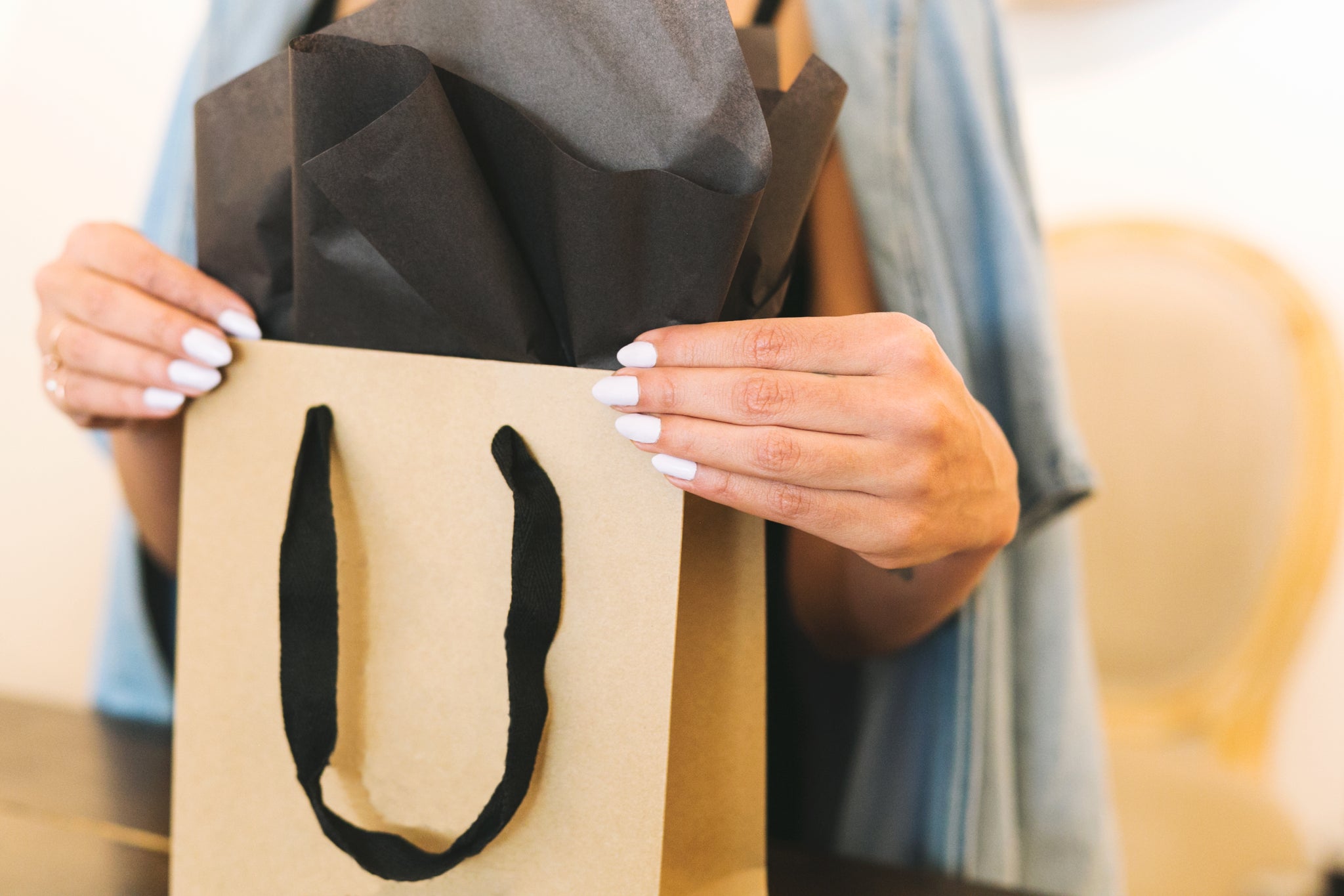 A shopping back with a black gift package popping out - being hold by a woman with white nails.