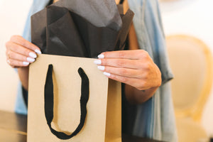 A shopping back with a black gift package popping out - being hold by a woman with white nails.