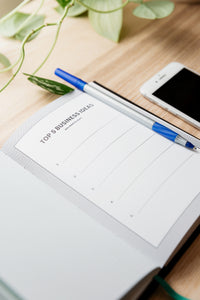 A picture of an open book with a 'to do list' on it, a blue pen and a phone on a wooden board.